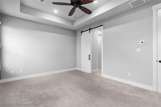 unfurnished bedroom with light carpet, ceiling fan, a barn door, and a raised ceiling