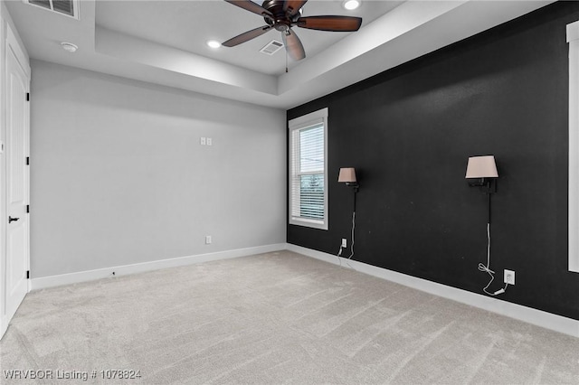 carpeted spare room with ceiling fan and a raised ceiling