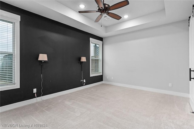 empty room with light colored carpet, a raised ceiling, and ceiling fan