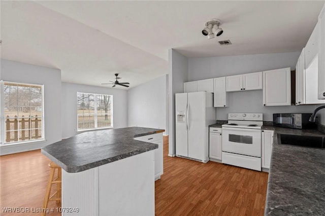 kitchen with white appliances, a sink, visible vents, vaulted ceiling, and dark countertops