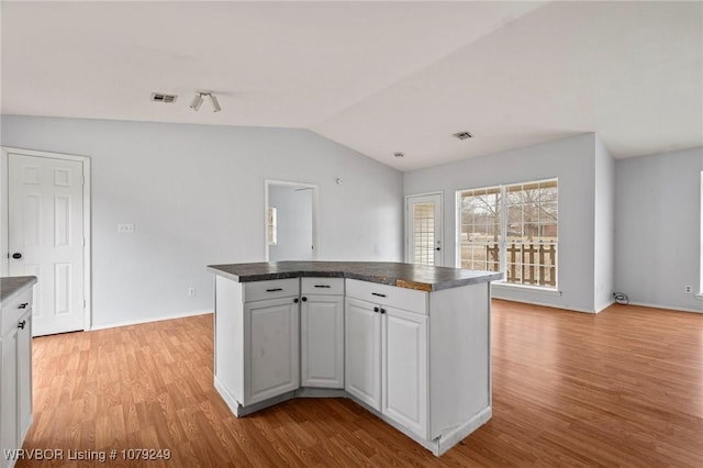 kitchen featuring dark countertops, a center island, vaulted ceiling, and light wood-style flooring