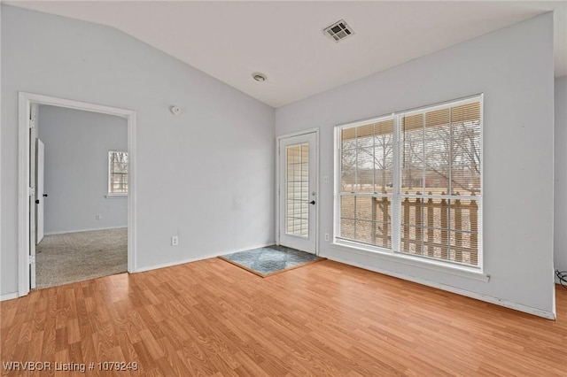 empty room featuring light wood-type flooring, lofted ceiling, and visible vents