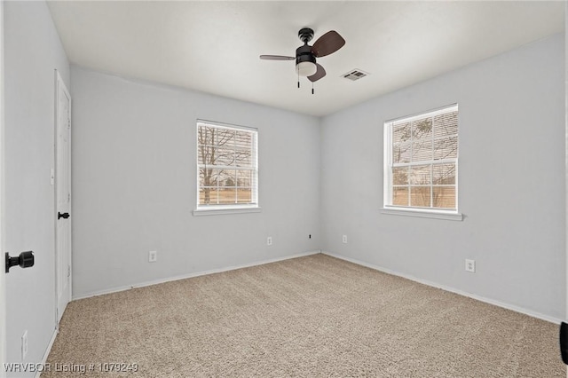 carpeted spare room with a healthy amount of sunlight, visible vents, and a ceiling fan