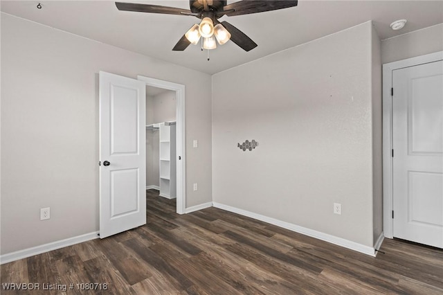 unfurnished bedroom with a closet, dark wood-style flooring, baseboards, and a spacious closet