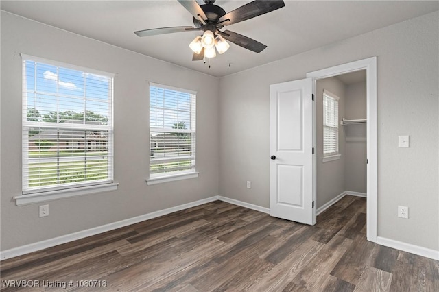 unfurnished bedroom with a ceiling fan, a closet, baseboards, dark wood-style flooring, and a walk in closet