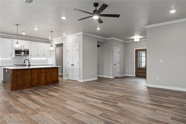 kitchen with open floor plan, a kitchen island with sink, stainless steel microwave, baseboards, and ceiling fan