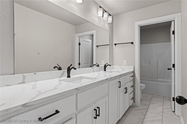 bathroom featuring toilet, marble finish floor, double vanity, and a sink