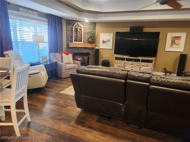 living room featuring dark hardwood / wood-style flooring, a tray ceiling, and a fireplace