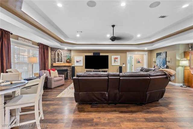 living room featuring a tray ceiling, dark wood-type flooring, and a large fireplace