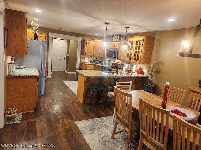 kitchen with pendant lighting, light stone counters, kitchen peninsula, stainless steel appliances, and dark wood-type flooring