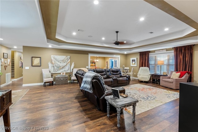 living room with ceiling fan, a tray ceiling, and dark hardwood / wood-style flooring