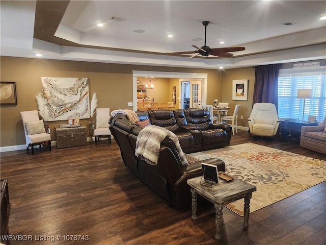 living room with a raised ceiling, dark wood-type flooring, and ceiling fan