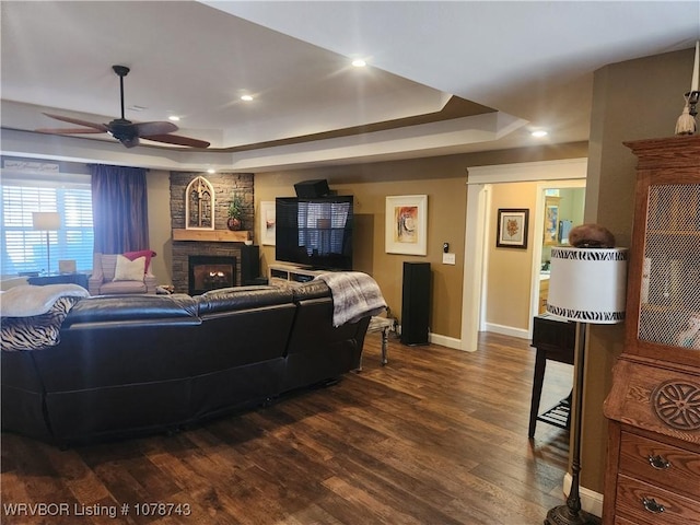 living room featuring ceiling fan, a large fireplace, dark hardwood / wood-style flooring, and a tray ceiling