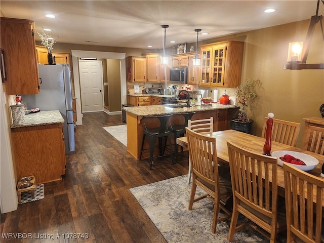 kitchen featuring appliances with stainless steel finishes, light stone counters, dark hardwood / wood-style flooring, decorative light fixtures, and kitchen peninsula