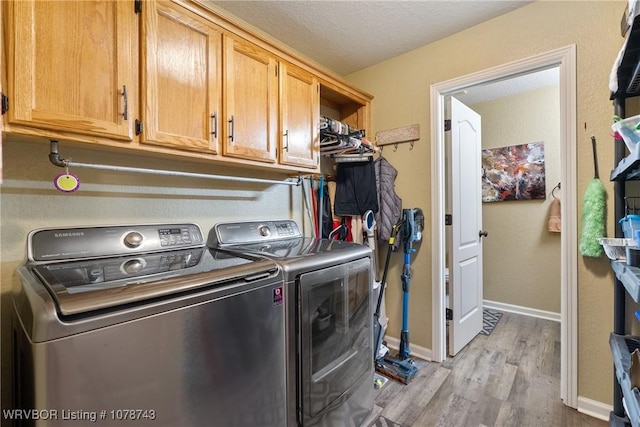 washroom featuring cabinets, washing machine and clothes dryer, a textured ceiling, and light hardwood / wood-style flooring