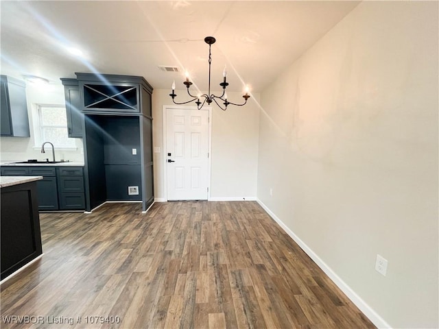 unfurnished dining area featuring dark wood finished floors, visible vents, an inviting chandelier, a sink, and baseboards