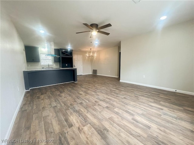 unfurnished living room featuring ceiling fan with notable chandelier, a sink, baseboards, and wood finished floors