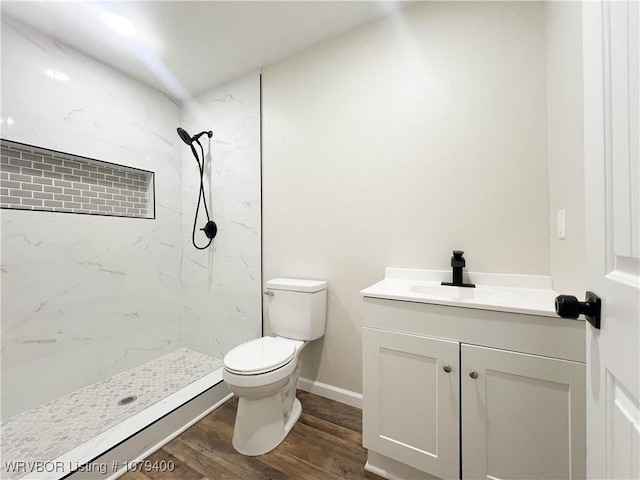 bathroom featuring toilet, wood finished floors, vanity, baseboards, and tiled shower