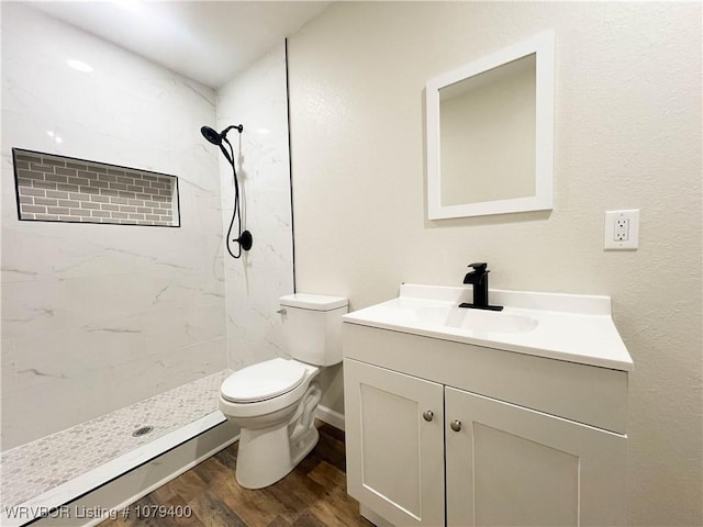 bathroom with toilet, tiled shower, wood finished floors, and vanity