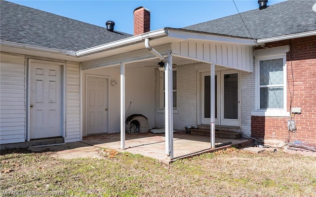 property entrance featuring brick siding, a chimney, roof with shingles, and a patio