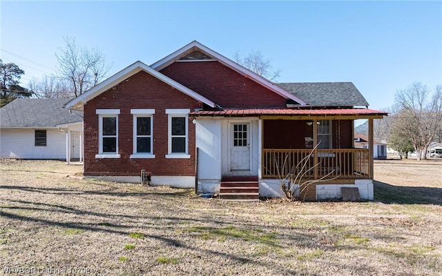 view of front facade featuring covered porch, brick siding, a front lawn, and a shingled roof