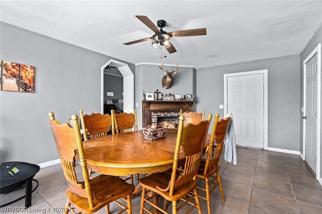 dining space with ceiling fan, baseboards, a textured ceiling, dark tile patterned flooring, and a brick fireplace
