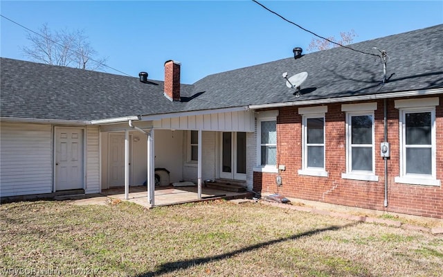 rear view of house featuring a patio area, a chimney, a lawn, and roof with shingles