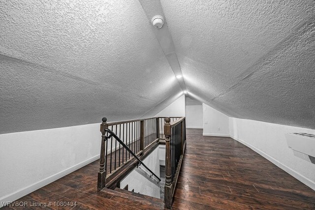 additional living space with wood-type flooring, lofted ceiling, a textured ceiling, and baseboards
