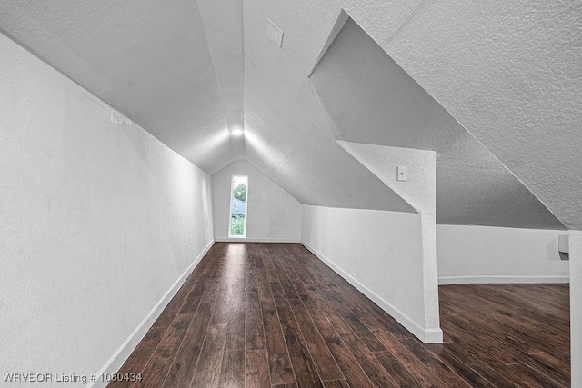 additional living space with wood-type flooring, vaulted ceiling, a textured ceiling, and baseboards