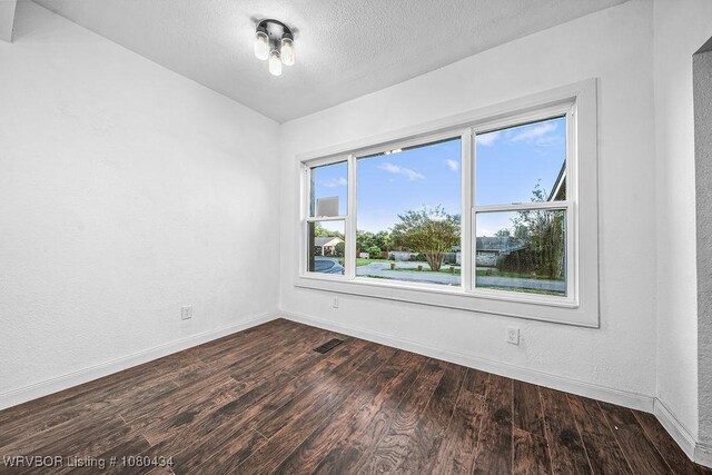 empty room featuring baseboards, visible vents, a textured ceiling, and dark wood finished floors