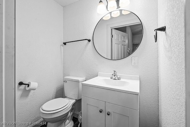 bathroom featuring toilet, a textured wall, and vanity