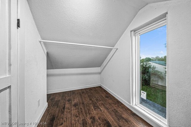 additional living space featuring a textured ceiling, vaulted ceiling, baseboards, a textured wall, and hardwood / wood-style flooring