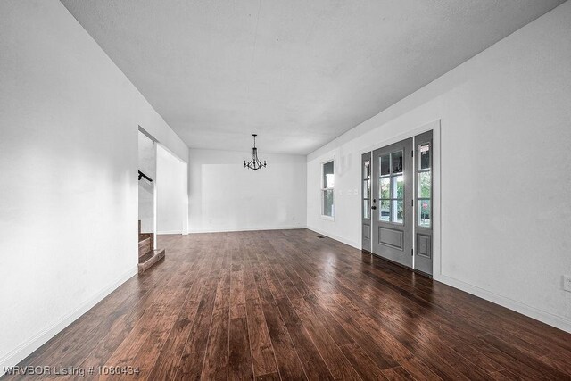 unfurnished room with baseboards, a notable chandelier, wood finished floors, and stairs