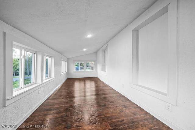 spare room featuring a textured ceiling, dark wood finished floors, vaulted ceiling, baseboards, and a textured wall