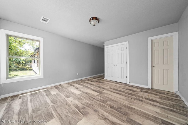 unfurnished bedroom featuring wood finished floors, baseboards, a closet, and a textured ceiling