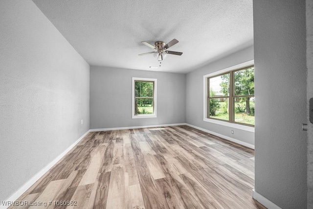 unfurnished room with healthy amount of natural light, ceiling fan, wood finished floors, a textured ceiling, and a textured wall