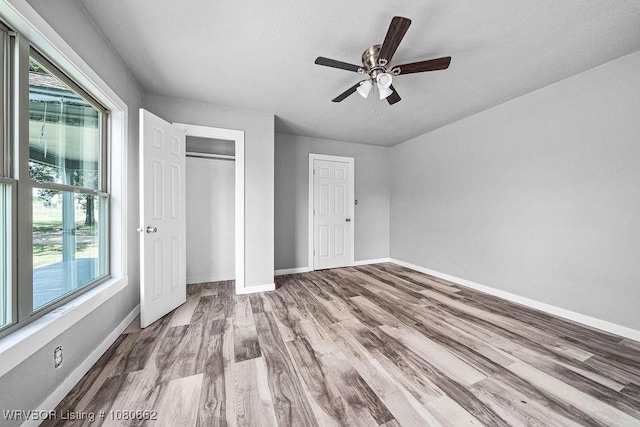 unfurnished bedroom with multiple windows, wood finished floors, baseboards, and a textured ceiling