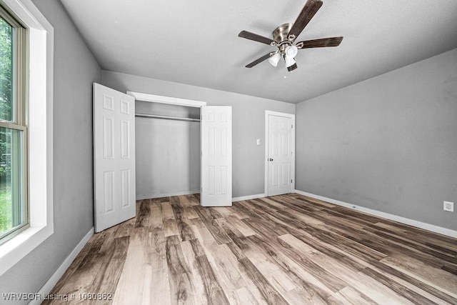 unfurnished bedroom featuring multiple windows, wood finished floors, a closet, and baseboards