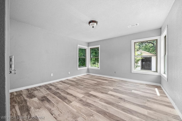 empty room with a textured ceiling, healthy amount of natural light, wood finished floors, baseboards, and a textured wall