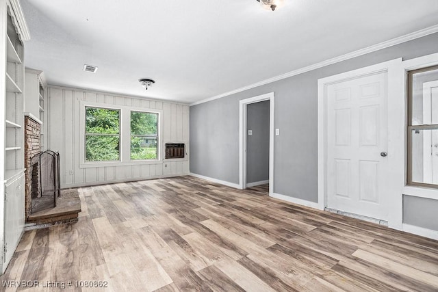 unfurnished living room with heating unit, wood finished floors, baseboards, crown molding, and a fireplace with raised hearth