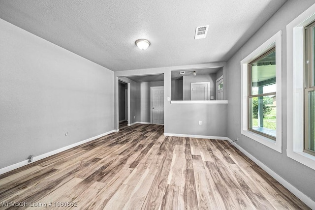 unfurnished living room with a textured ceiling, wood finished floors, and baseboards