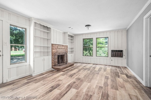 unfurnished living room featuring light wood-type flooring, ornamental molding, a fireplace, built in shelves, and heating unit