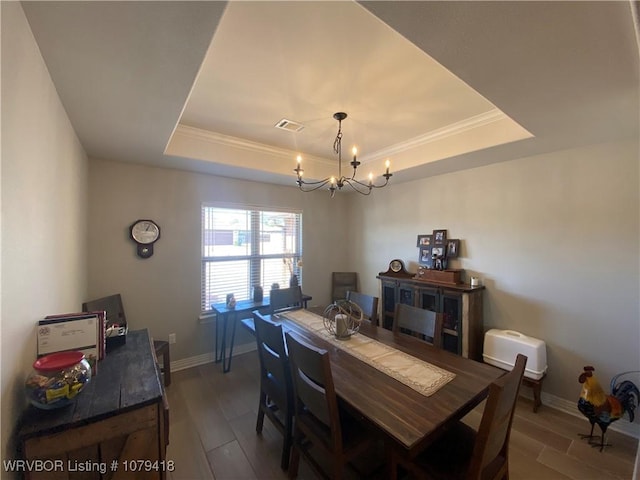 dining space featuring visible vents, baseboards, wood finished floors, an inviting chandelier, and a tray ceiling