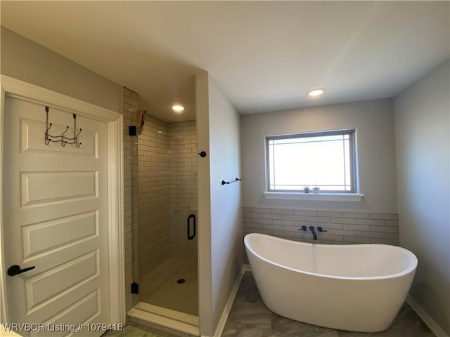 bathroom featuring a freestanding tub, recessed lighting, tile walls, baseboards, and a stall shower