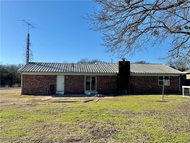 rear view of house with metal roof, brick siding, a chimney, and a lawn