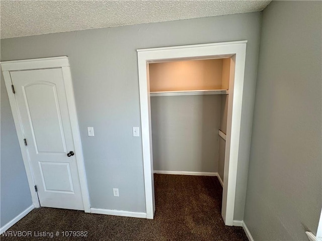 unfurnished bedroom featuring a textured ceiling, dark colored carpet, a closet, and baseboards