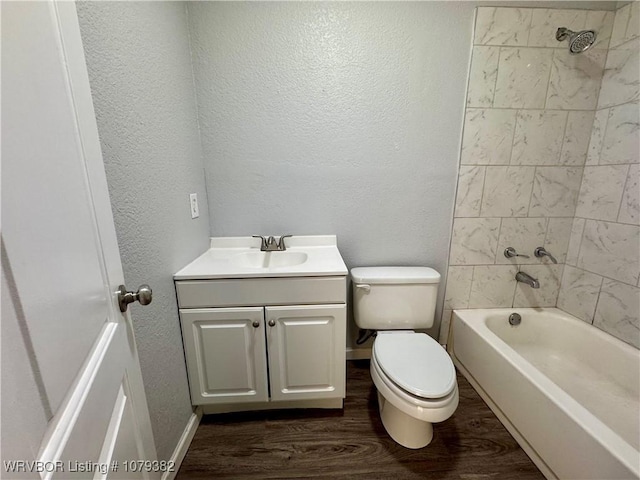 bathroom with a textured wall, toilet, wood finished floors, vanity, and shower / bathing tub combination