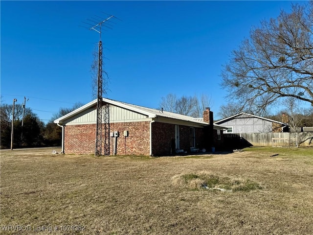 rear view of property with brick siding, a chimney, fence, and a yard