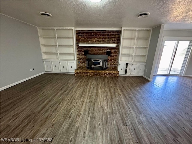 unfurnished living room featuring built in shelves, dark wood-style flooring, a wood stove, a textured ceiling, and baseboards