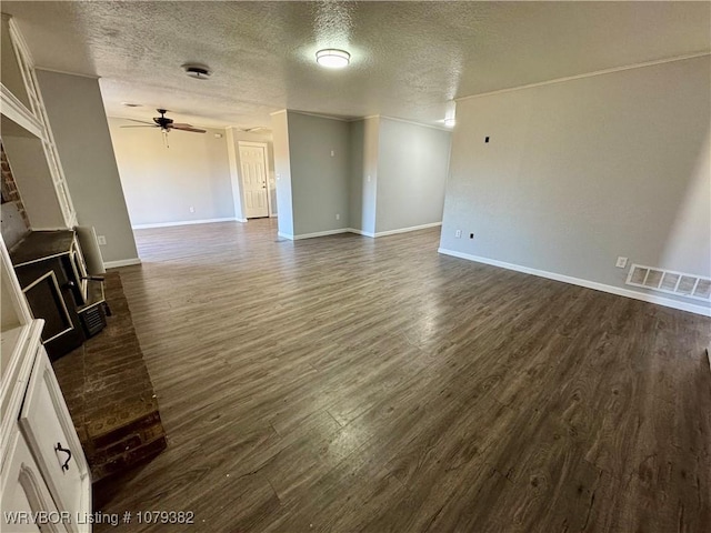 unfurnished living room featuring ceiling fan, a textured ceiling, visible vents, baseboards, and dark wood finished floors